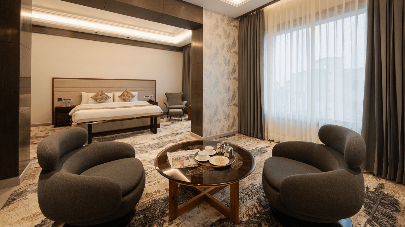A spacious guest suite with a king-sized bed and two modern grey armchairs around a coffee table at Ananta Express, Katra.