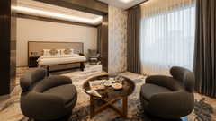 A spacious guest suite with a king-sized bed and two modern grey armchairs around a coffee table at Ananta Express, Katra.