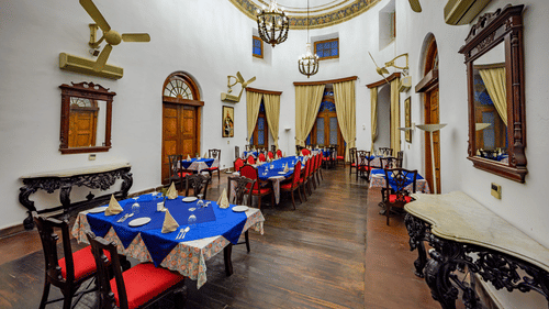 An indoor dining area with arranged tables, chairs, wall decor, and high ceiling in a heritage-style setting.