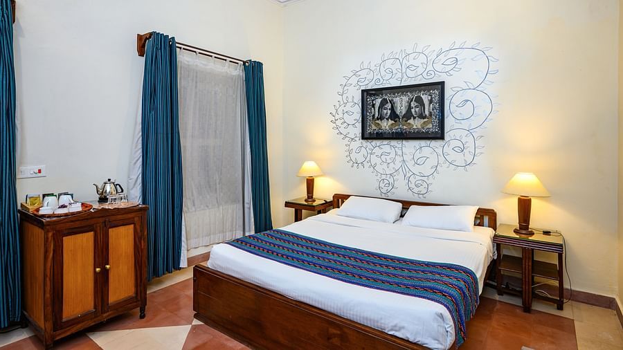 A bedroom with a bed, artwork on the wall, curtains, and a cabinet at Tijara Fort-Palace - 19th Century, Alwar.