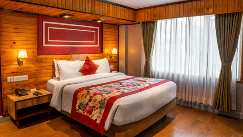 A room with rich wooden interiors, a queen-sized bed with floral bedding and red accents, side lamps, and a large window draped in soft curtains - Mount Hotels