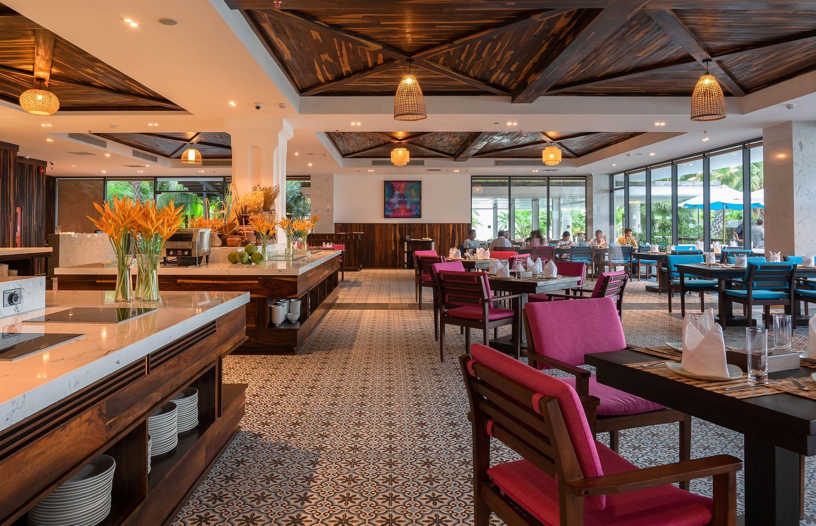 A well lit restaurant at our hotel with maroon coloured cushions on wooden chairs placed around the tables and a bar counter - Alibu Resort Nha Trang 