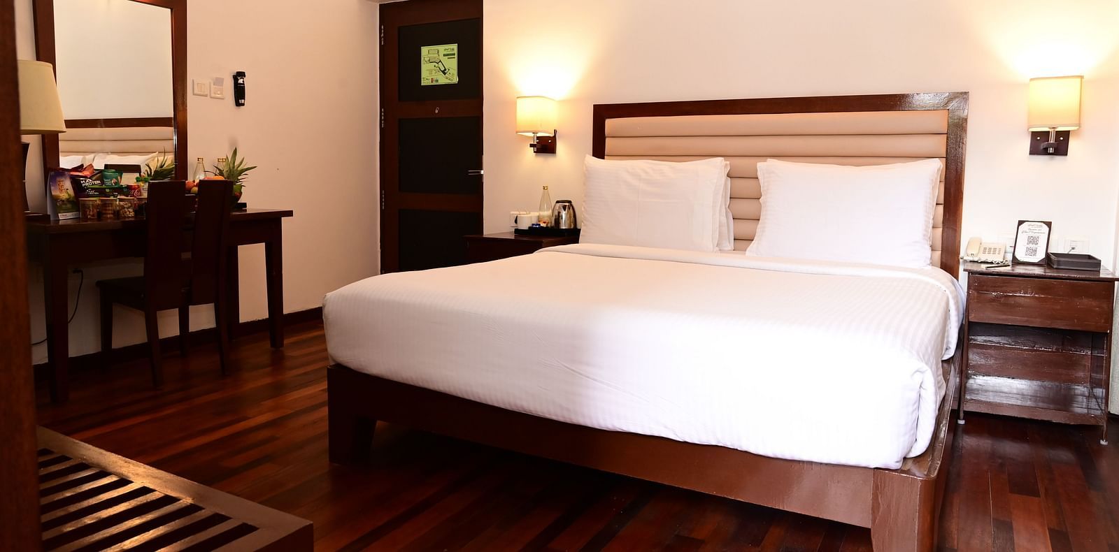 An image of a room with a king size bed, bed side table, lamps, dressing table, and a chair - GReaT trails Kodaikanal by GRT Hotels