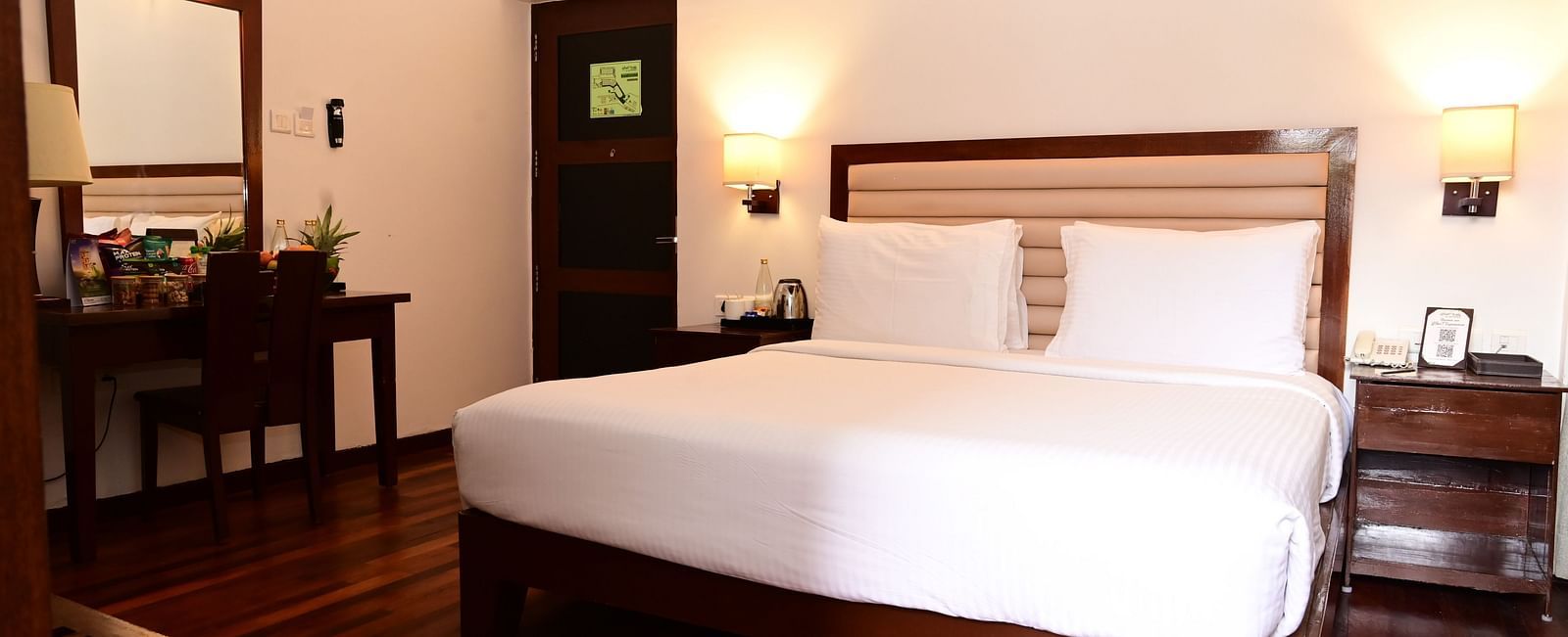 An image of a room with a king size bed, bed side table, lamps, dressing table, and a chair - GReaT trails Kodaikanal by GRT Hotels