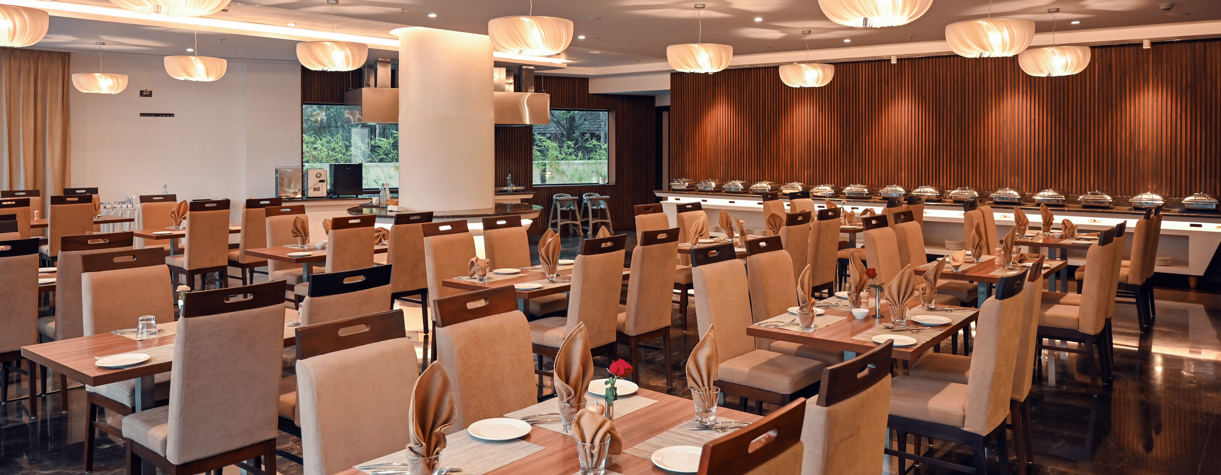 A sitting area at the multi-cuisine restaurant with tables, chairs, and lights at Dimora, Kozhikode.