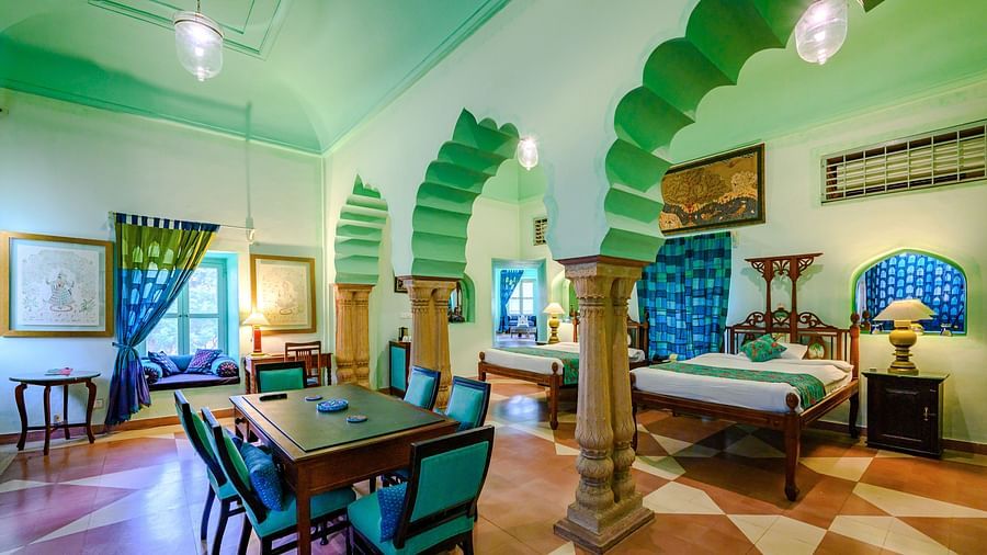 A spacious room with a bed, a dining table, seating, and decorative arched alcoves at Tijara Fort-Palace - 19th Century, Alwar.