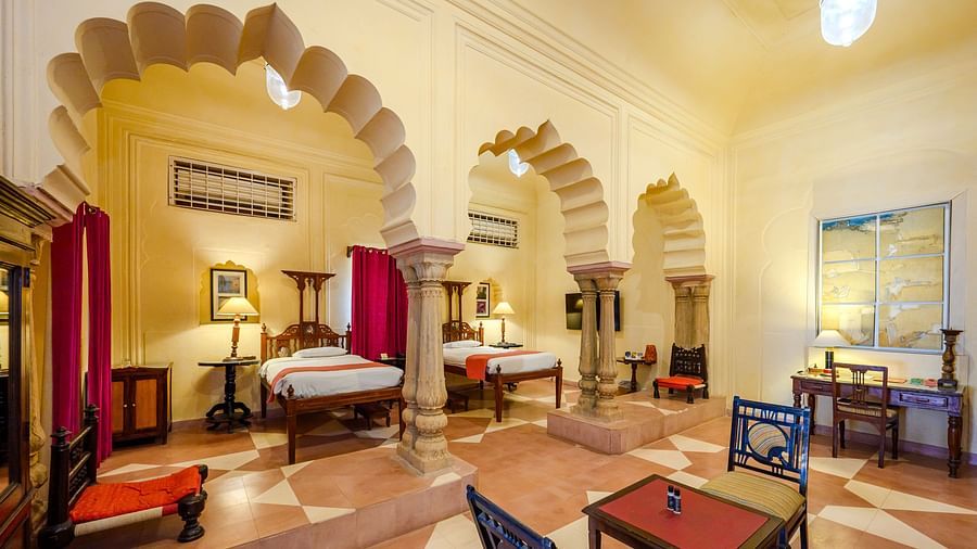 A spacious room with two single beds, seating areas, and arched architectural details at Tijara Fort-Palace - 19th Century, Alwar.