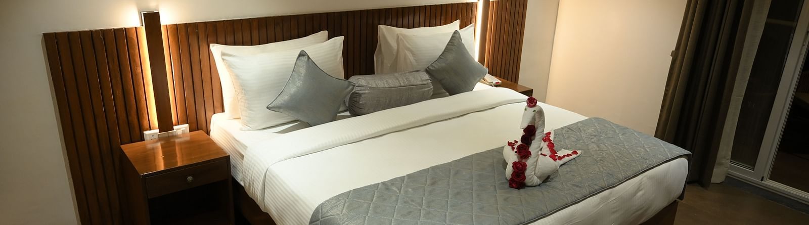 A doubled bed with a decorated towel at Deluxe room at  Mango Leaf Lake Resort, Pune