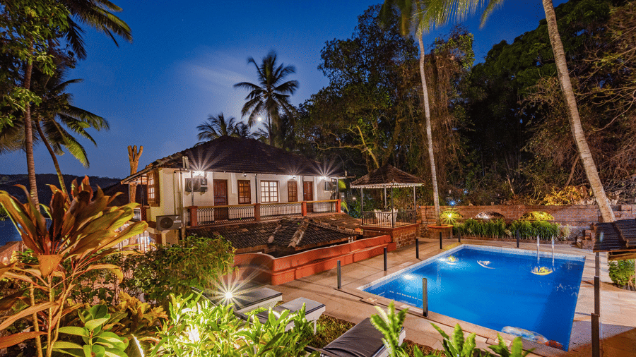 Tropical resort with a swimming pool surrounded by palm trees at night.