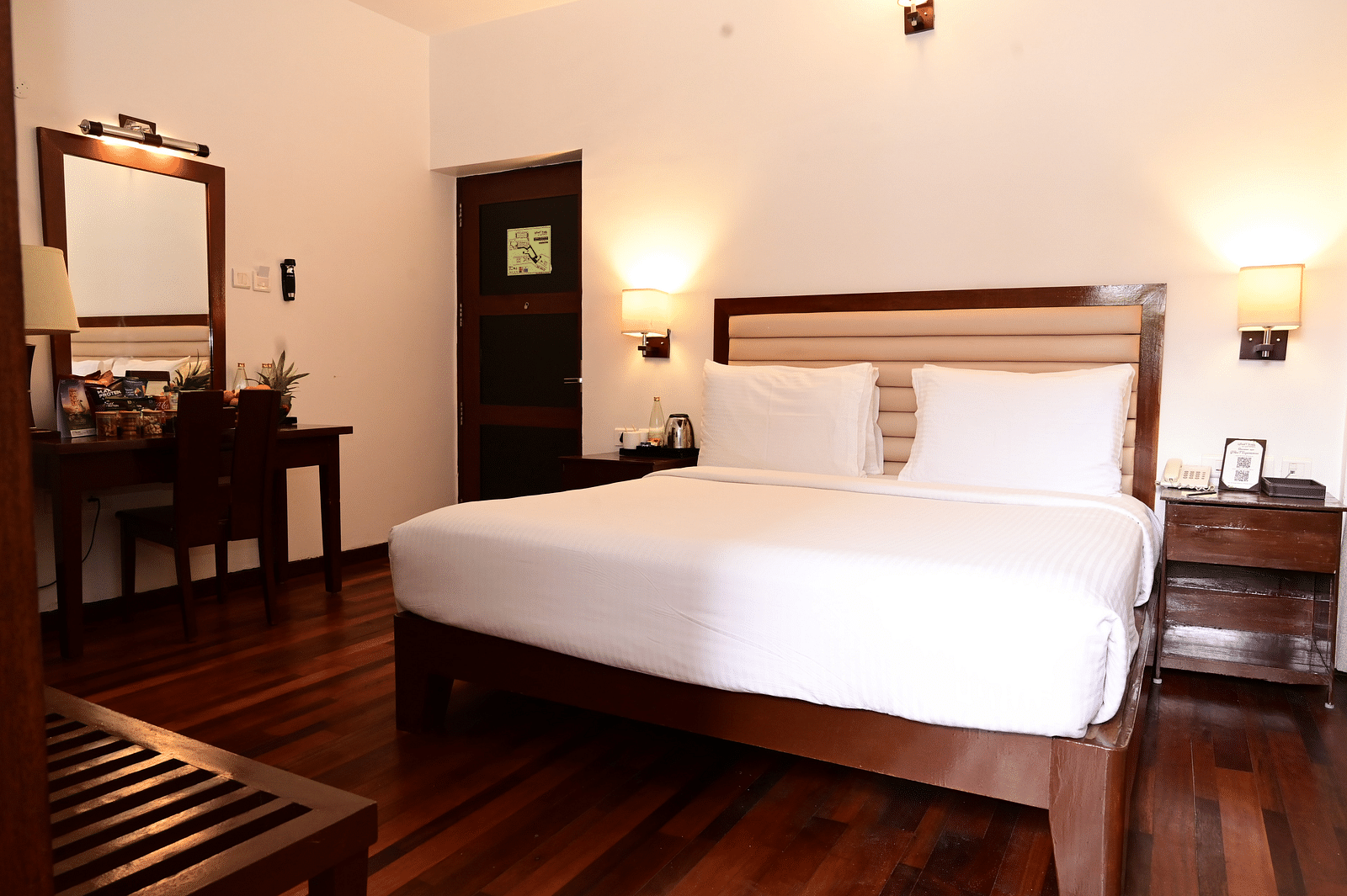 An image of a room with a king size bed, bed side table, lamps, dressing table, and a chair - GReaT trails Kodaikanal by GRT Hotels