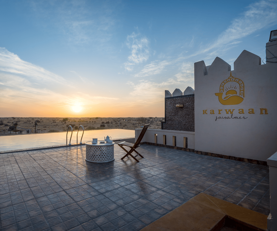 A foldable chair and a small table is placed near the pool - Karwaan Jaisalmer