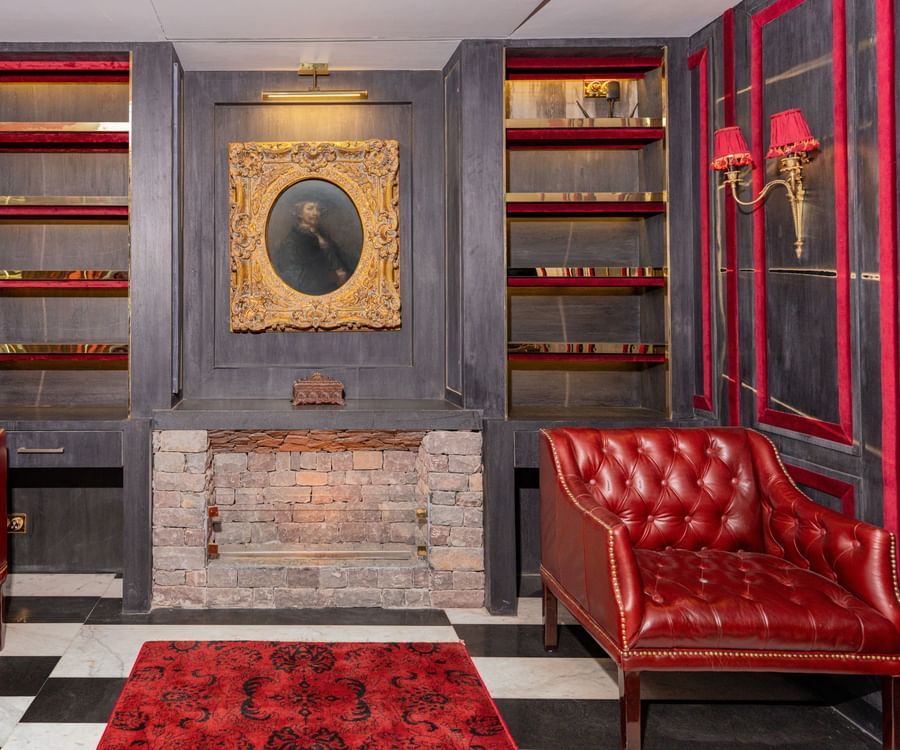 A couple of beautiful red chairs placed in front of a fire place with a vintage painting hanging on the wall - The Manor Luxury Hotel, Shimla