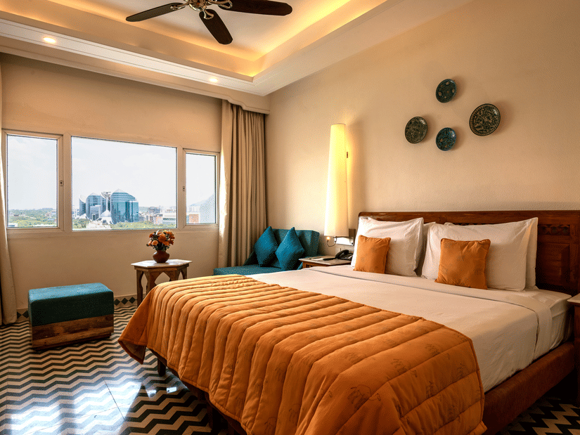 Club room's bedroom at Clarks Group of Hotels featuring a king-size bed, patterned flooring, warm lighting, seating area and city view window.