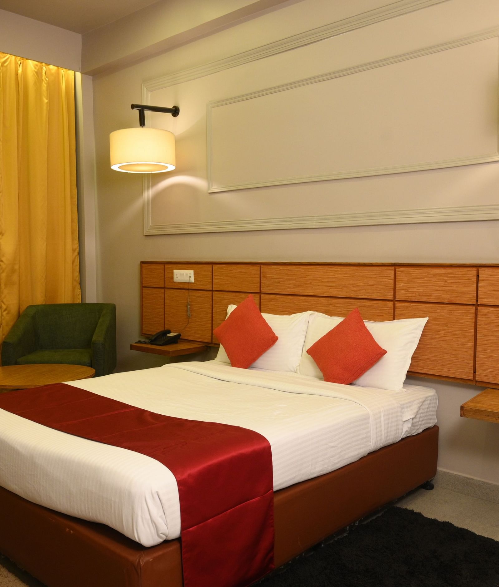 A room at Max Hotel Prayagraj, featuring a bed with white linens and red accents, a wooden headboard, and a small bedside table.