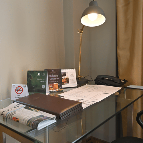 A glass desk in a room with a lamp, books, and a chair at Polo Hotel Agartala