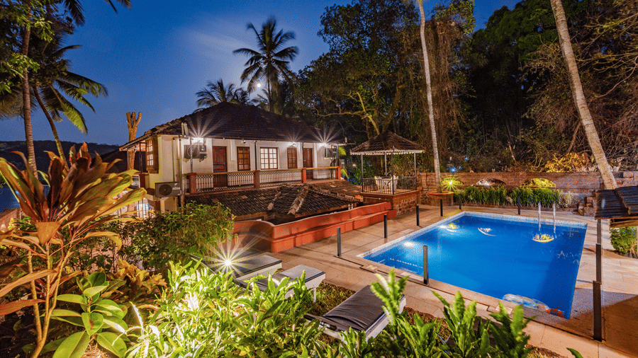 Tropical resort with a swimming pool surrounded by palm trees at night.