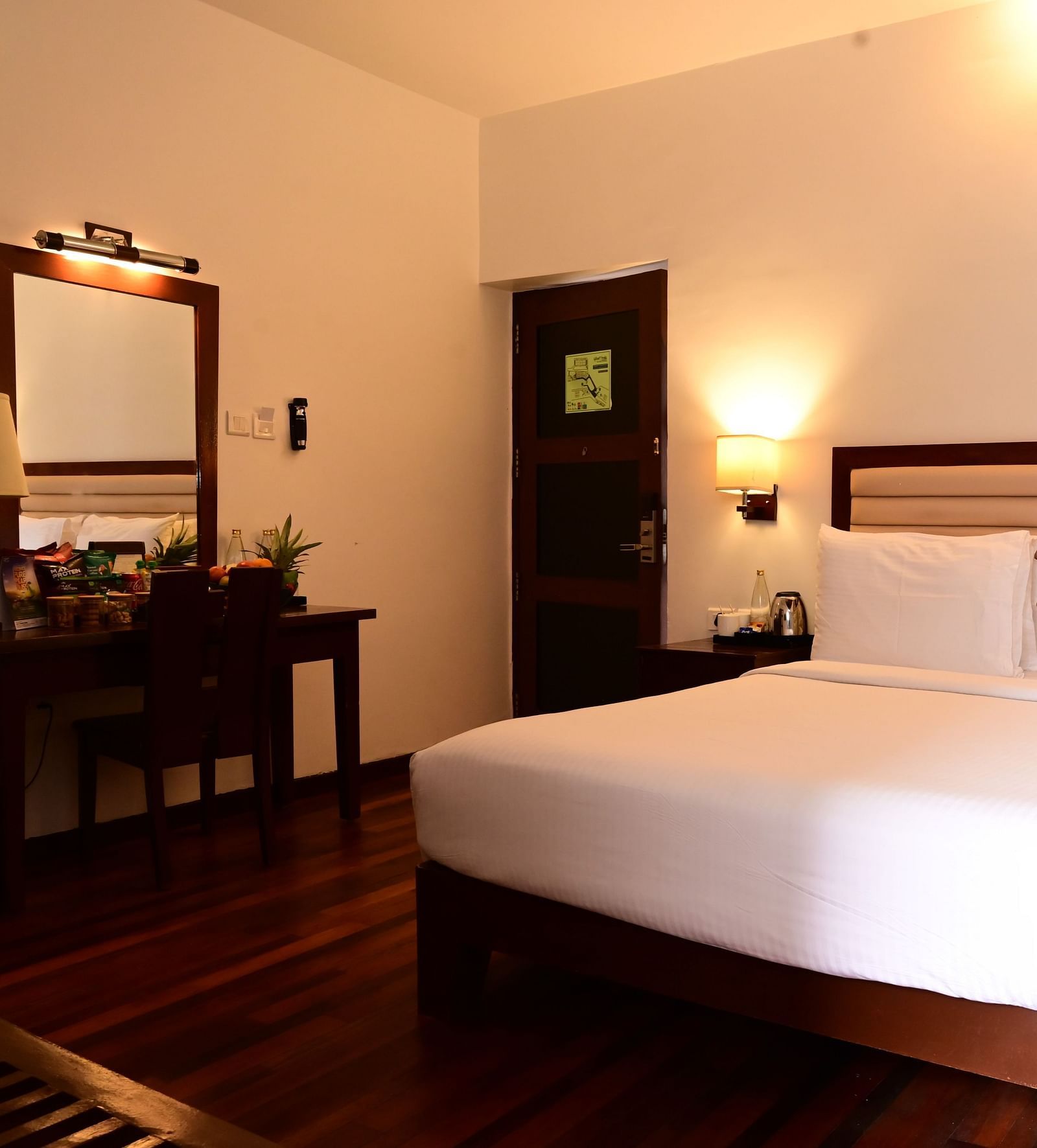 An image of a room with a king size bed, bed side table, lamps, dressing table, and a chair - GReaT trails Kodaikanal by GRT Hotels