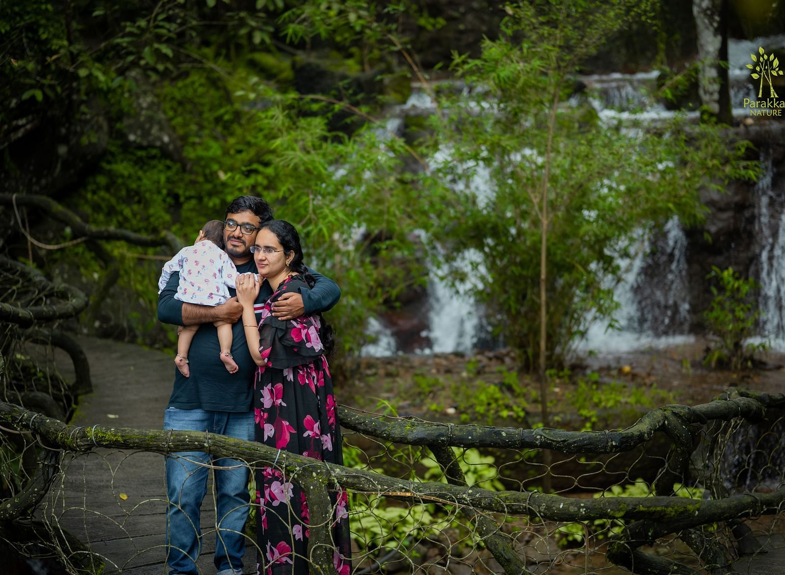 A couple standing with a baby in front of the Artificial waterfall at Parakkat Nature Hotel and Resorts, Munnar