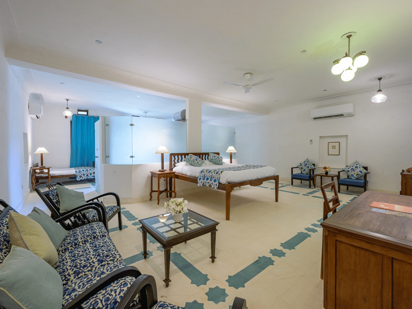 A spacious room with a bed, bedside tables with lamps, multiple seating areas with sofas and chairs around tables, and patterned flooring at Tijara Fort-Palace - 19th Century, Alwar