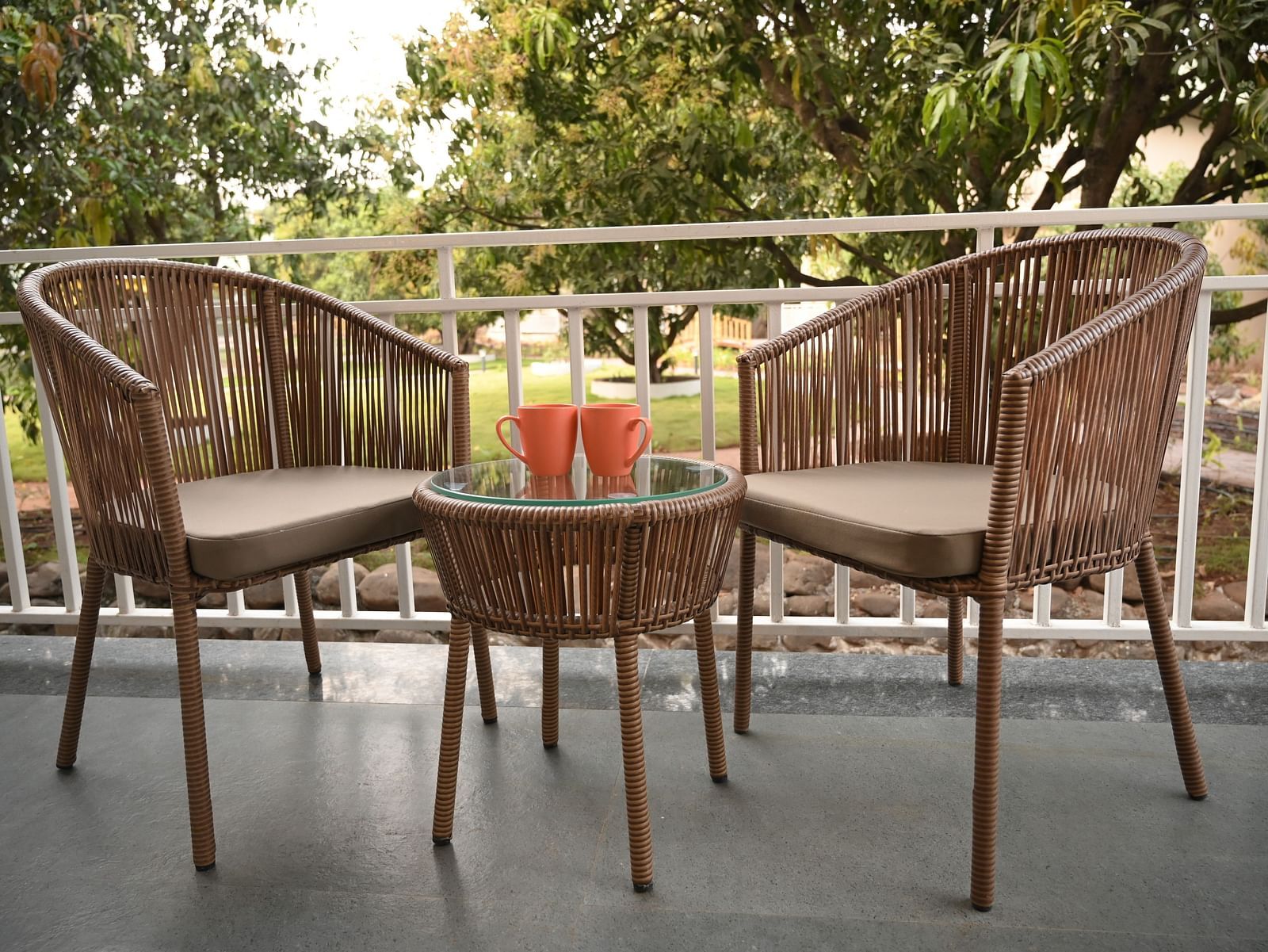 Two chairs with a small tea table with juice glasses kept on it outside  the Deluxe Cottage at Mango Leaf Lake Resort, Pune