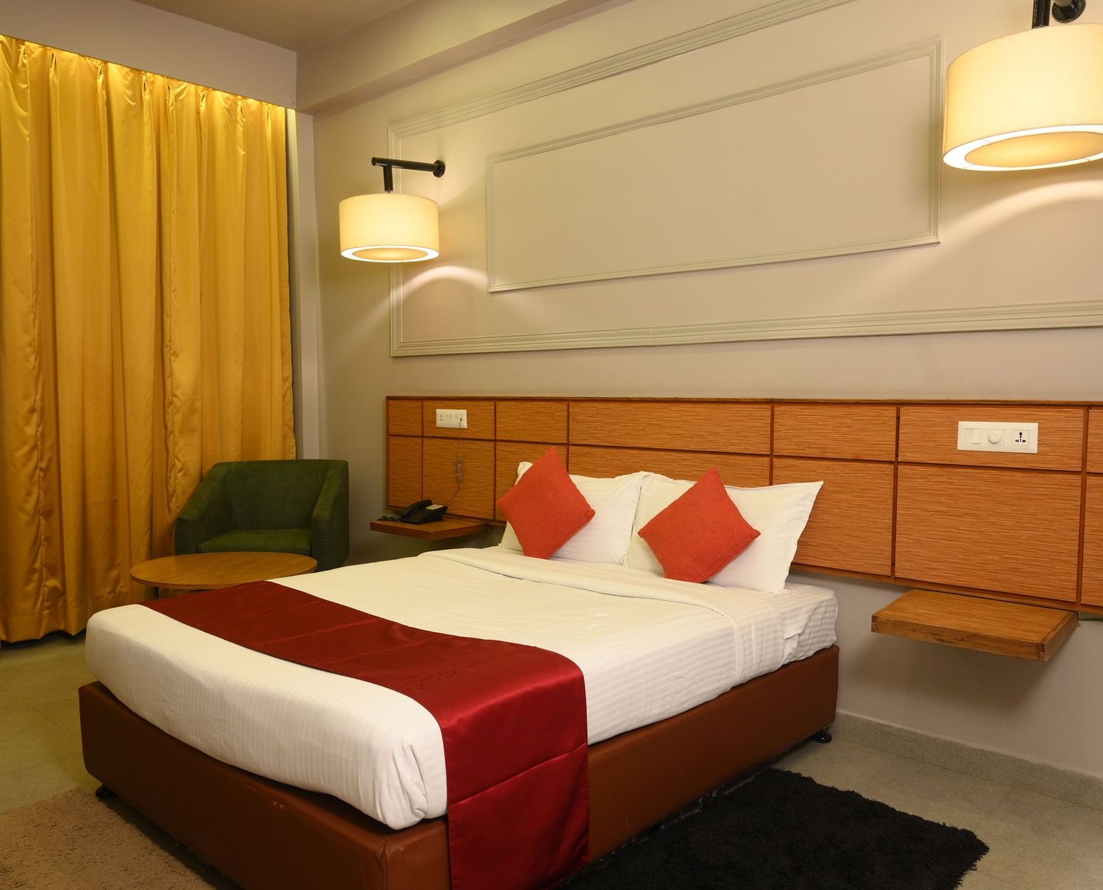A room at Max Hotel Prayagraj, featuring a bed with white linens and red accents, a wooden headboard, and a small bedside table.