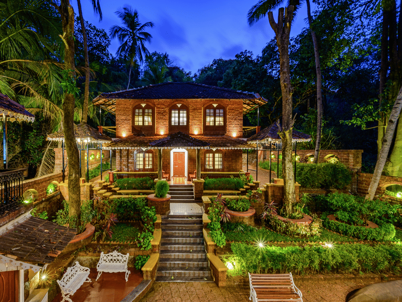 A far out view of Neemranas Three Waters facade with trees, steps and twilight sky in view for the perfect Cabo De Rama Stay.