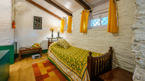 A single bed at the Lemon Room with curtains on the windows - Ramgarh Bungalows, Nainital.