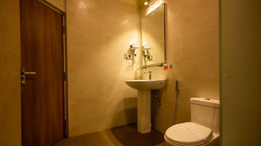 A well-lit modern bathroom with beige tiles, featuring a sink, wall-mounted mirror, toilet and amenities like hand soap and a hair dryer.