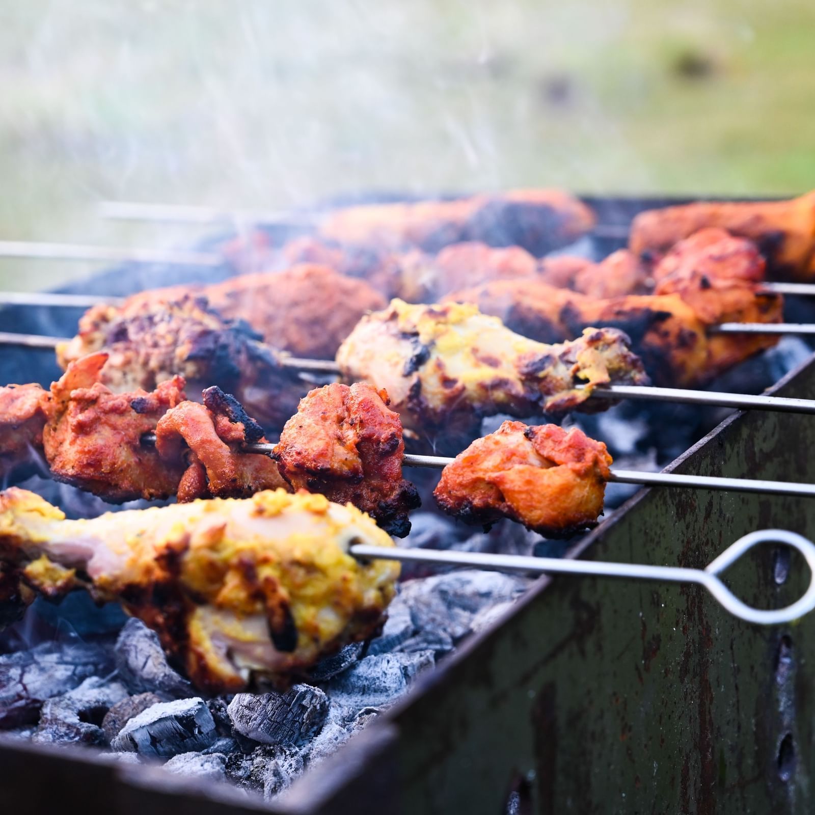 Delicious skewered meats cooking on a charcoal grill, with smoke rising | Diamond Parks, Pune