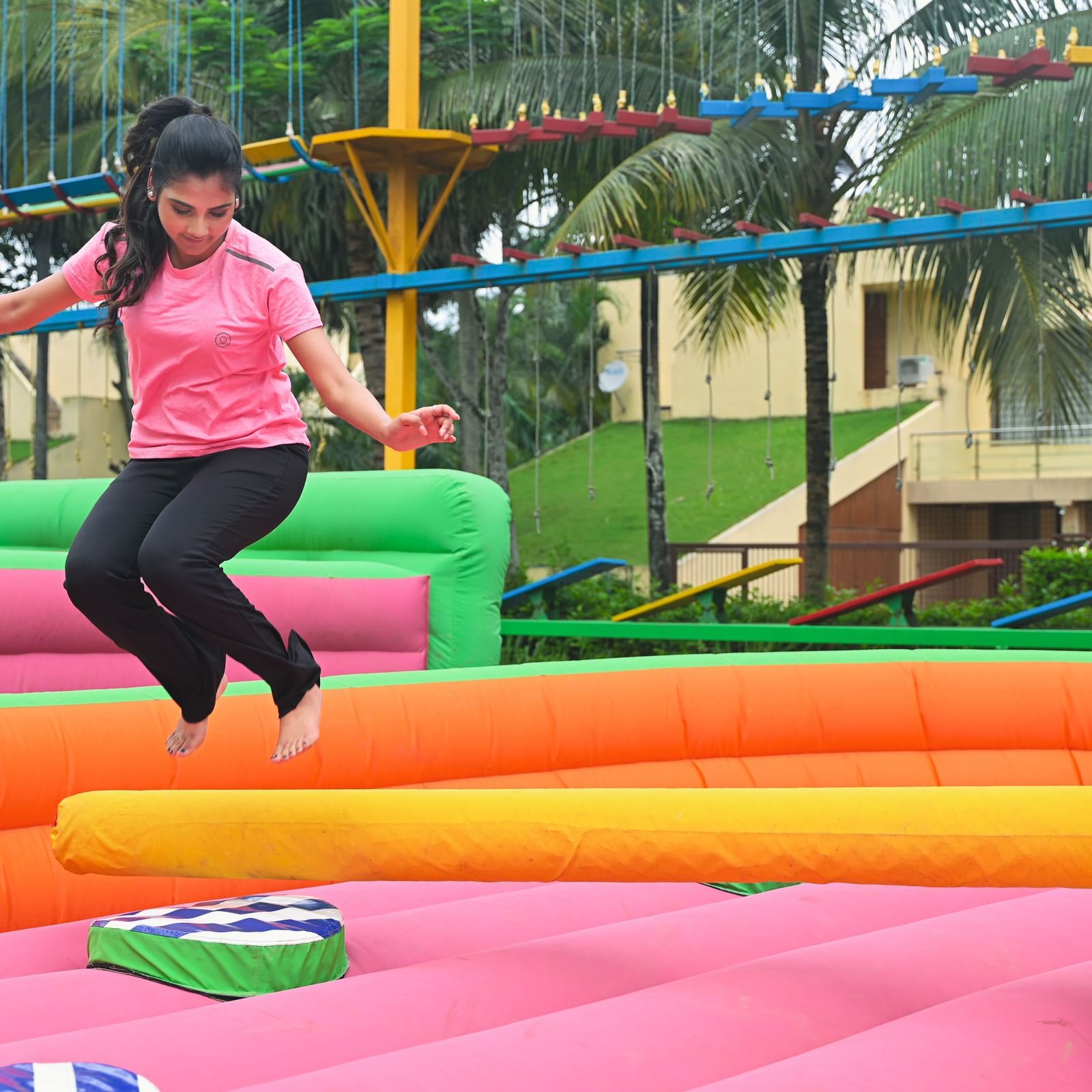 A person in a pink shirt jumps on a colorful inflatable structure outdoors