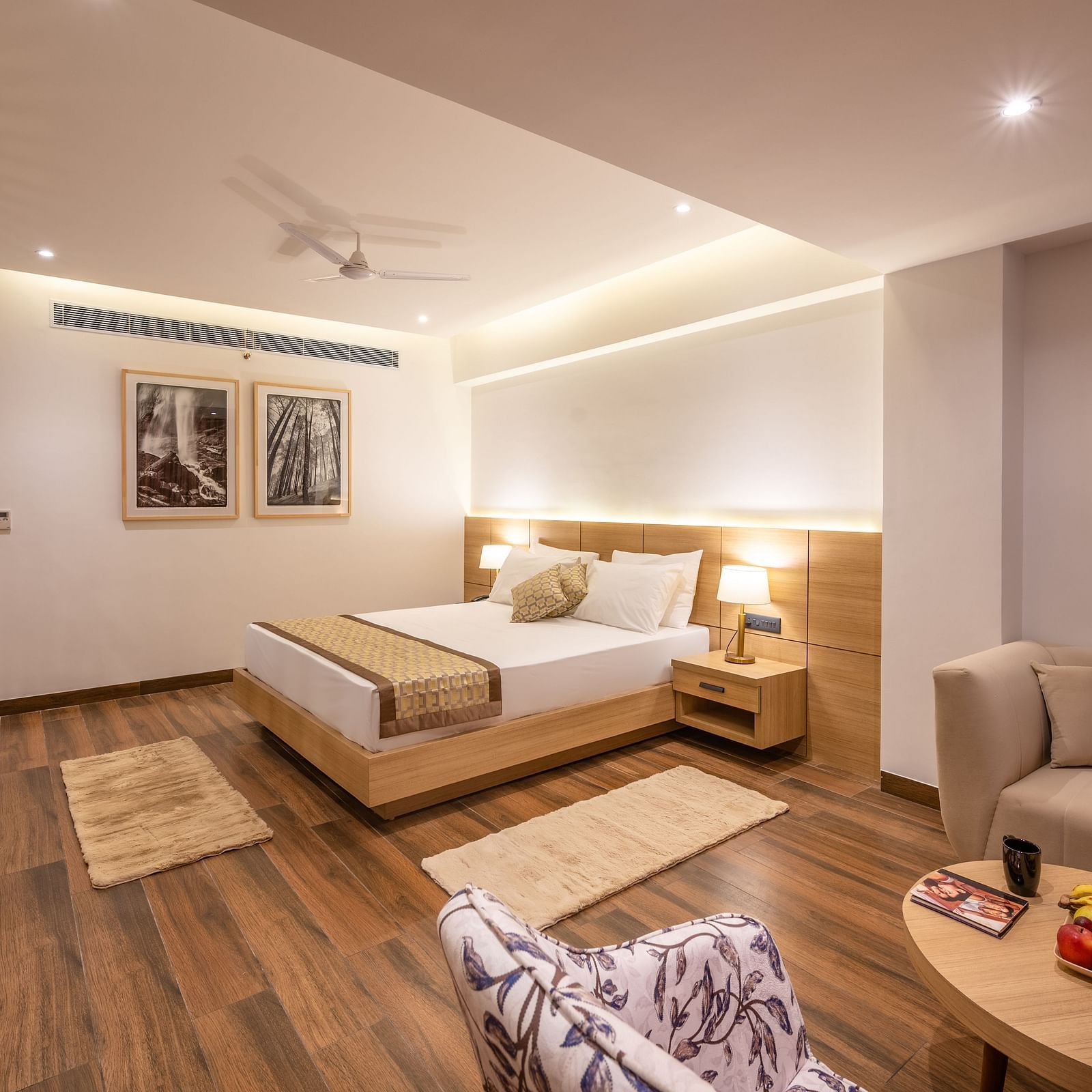 Side shot of Suite at Vishranti Resort, Dehradun featuring a king bed with side tables, a sofa, a TV, large window with curtains and bed lamps. 