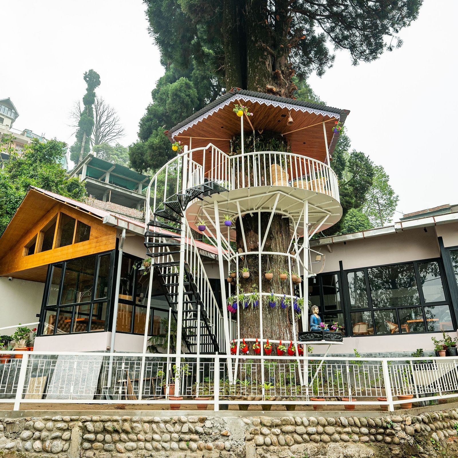 A multi-tiered, modern-rustic building with a spiral staircase, set against a backdrop of lush greenery- Arcadia Heritage Resort, Darjeeling