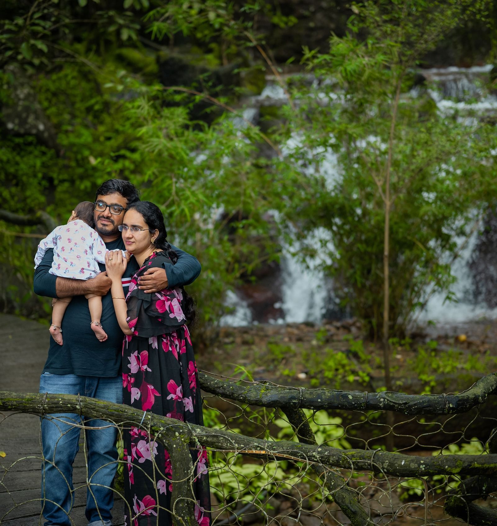 A couple standing with a baby in front of the Artificial waterfall at Parakkat Nature Hotel and Resorts, Munnar