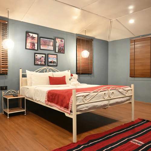 A spacious bedroom featuring a metal bed, a rug on wooden flooring, pendant lights, and framed artwork.