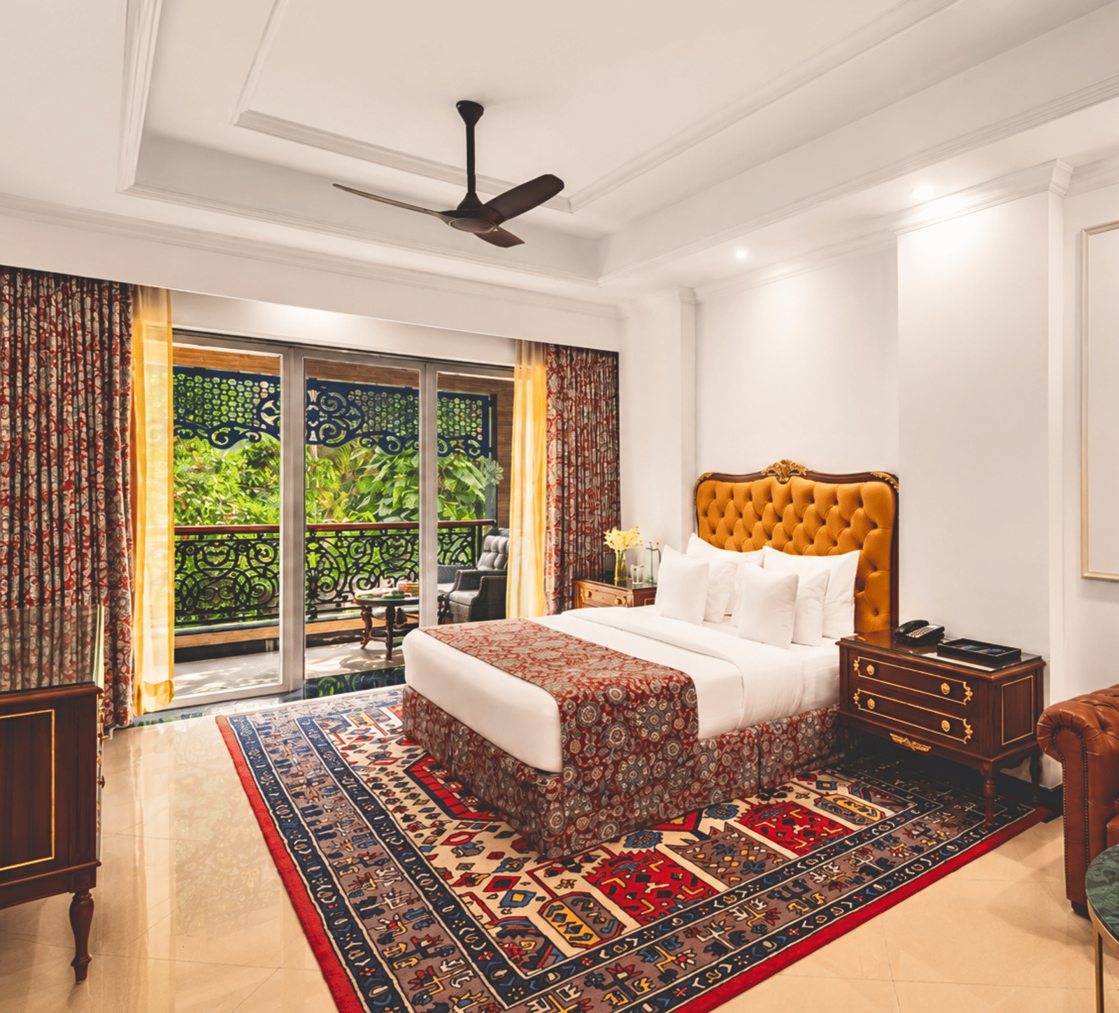 King bed room with a tufted leather headboard, a sofa, floral wall art and a balcony overlooking greenery at MAYFAIR Palm Beach Resort, Gopalpur-on-Sea.