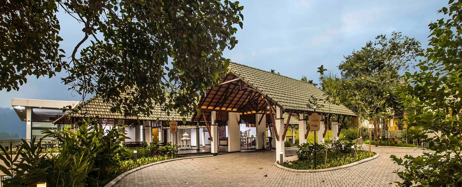 Lush foliage frames a building with a pitched roof and covered walkway - Great Trails Wayanad by GRT hotels.
