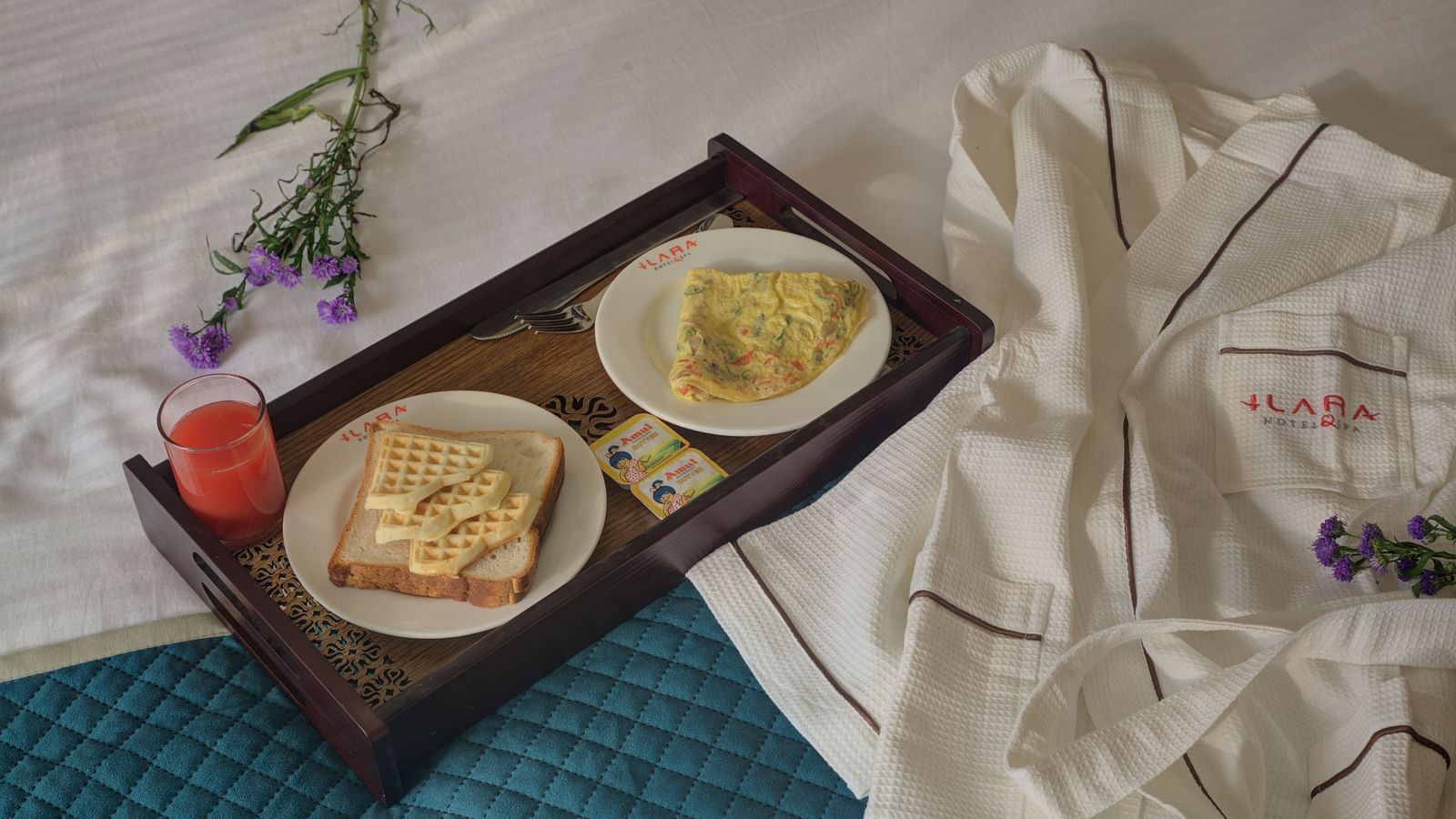 Breakfast tray with a neatly presented meal including eggs, bread, and a tomato, placed on a bed with a textured blue blanket at Ilara Hotels & Spa