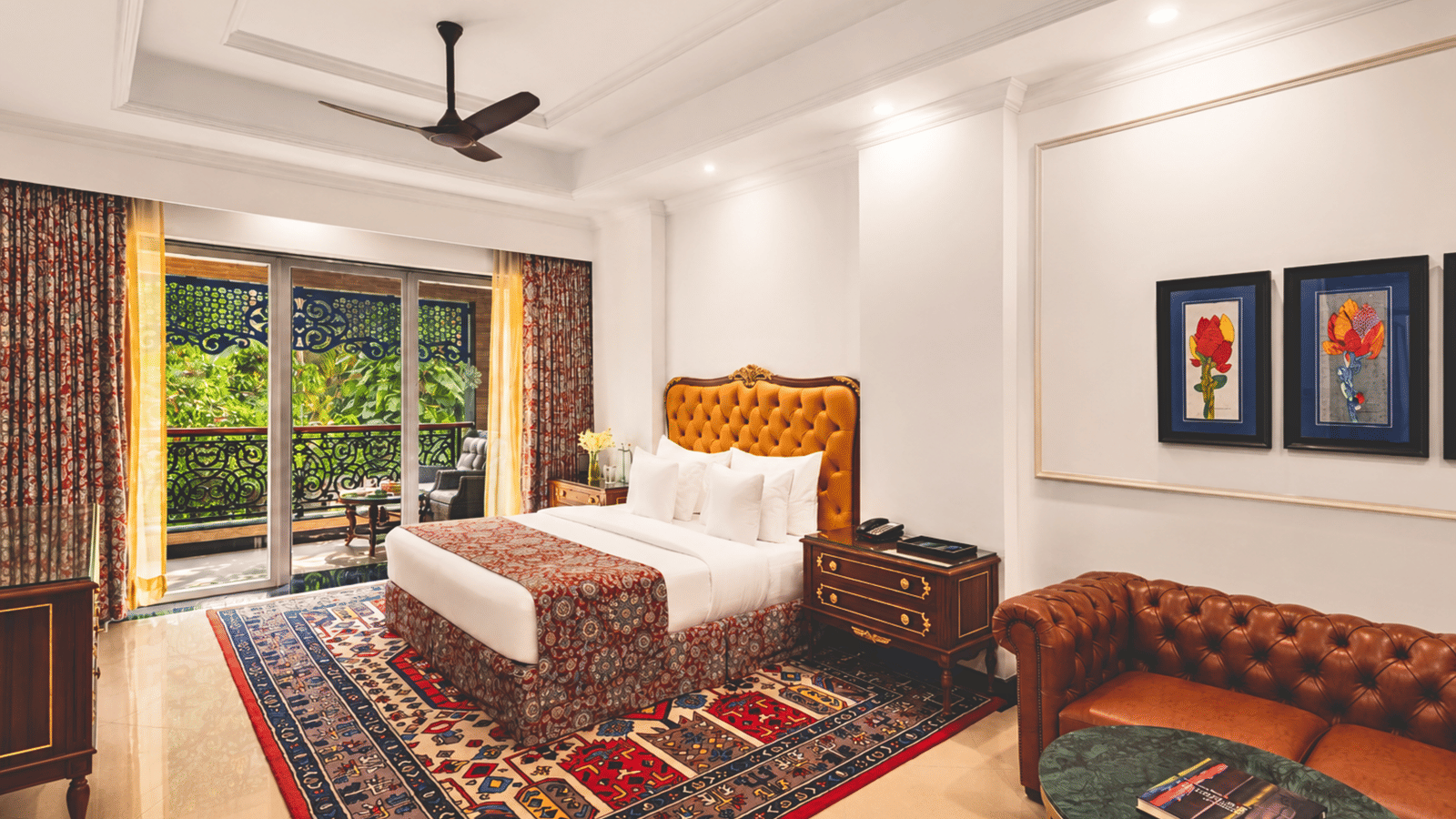 King bed room with a tufted leather headboard, a sofa, floral wall art and a balcony overlooking greenery at MAYFAIR Palm Beach Resort, Gopalpur-on-Sea.