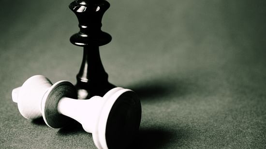 A black chess queen standing upright next to a toppled white king on a textured surface.