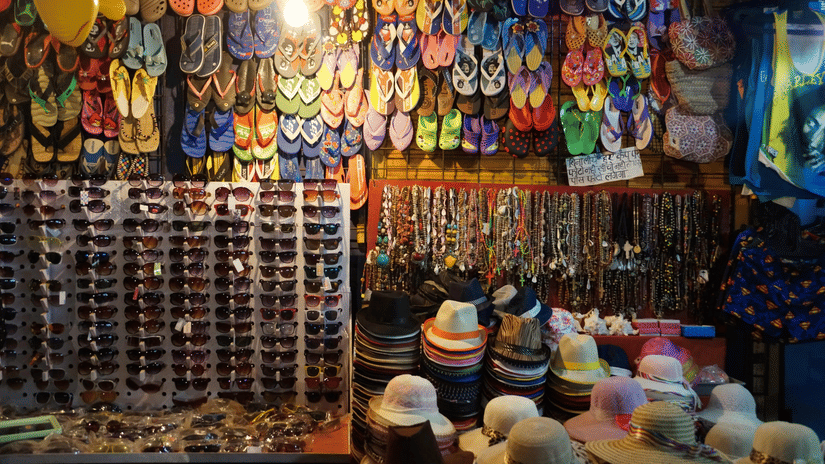 A colourful market stall filled with holiday accessories, featuring flip-flops, sunglasses, necklaces, and sun hats.