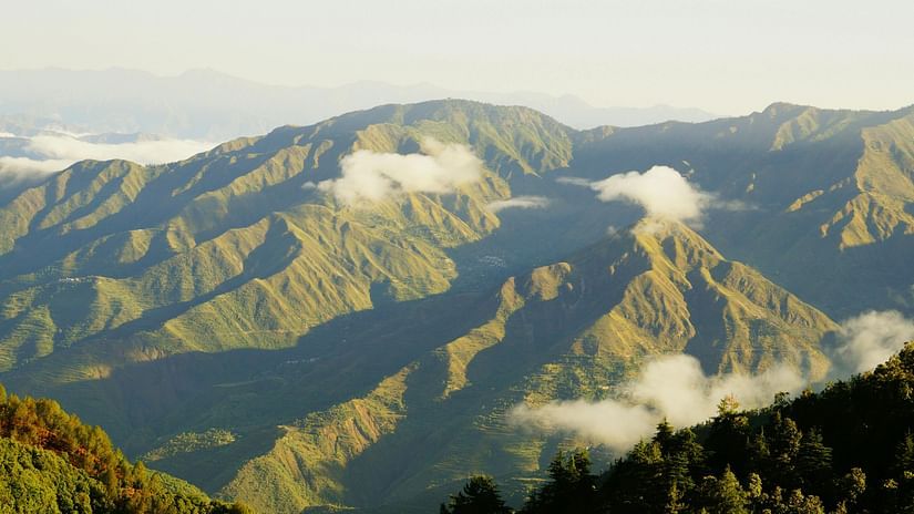 Aerial view of sunlit mountain ranges with rolling clouds.