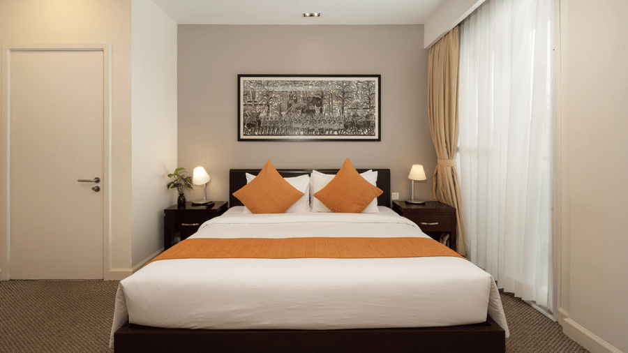 Penthouse bedroom at Central Mansions, Phnom Penh with a king bed, bedside lighting, and large windows.