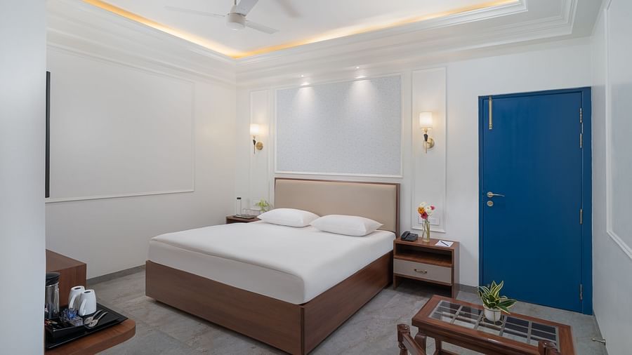 A spacious bed with bright, inviting lighting and a wooden table with a plant on it | Hotel Ganga Maiya