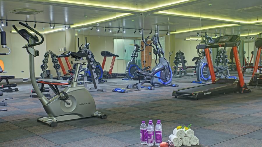 The gym area with various fitness equipment along with packaged drinking water and rolled towels kept on the floor at Ilara Hotels & Spa, Tada.