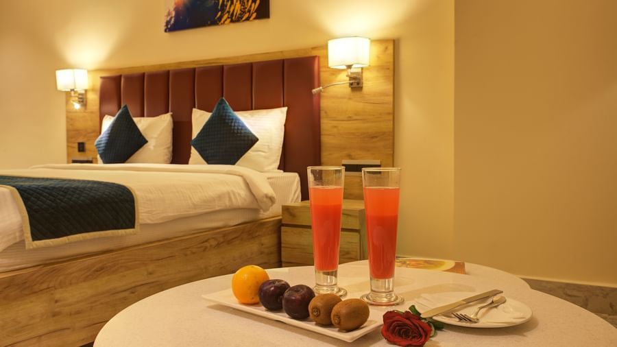 A coffee table light snacks and two tall glasses of fresh juice overlooking a plush double bed at the Junior Suite at Ilara Hotels & Spa, Tada.