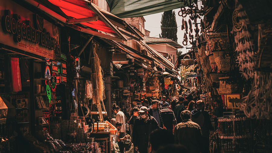 A crowded market lane with stalls shaded by red awnings in Johri Bazar, Jaipur