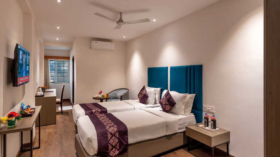 Lords Eco Inn deluxe bedroom with a large bed, a headboard, a ceiling fan, and simple wooden furniture.