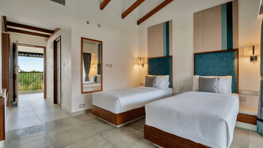 Interior of Twin Room at Mango Hill, Velankanni showing 2 beds, a mirror, and an entrance leading to a doorway.