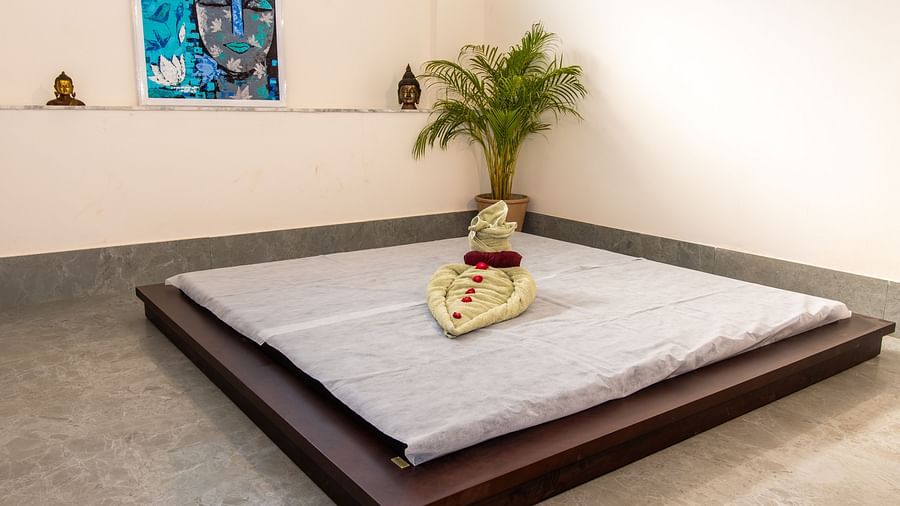 An image of a ground level wooden bed with towels decorated on top at Rajbagh Wellness