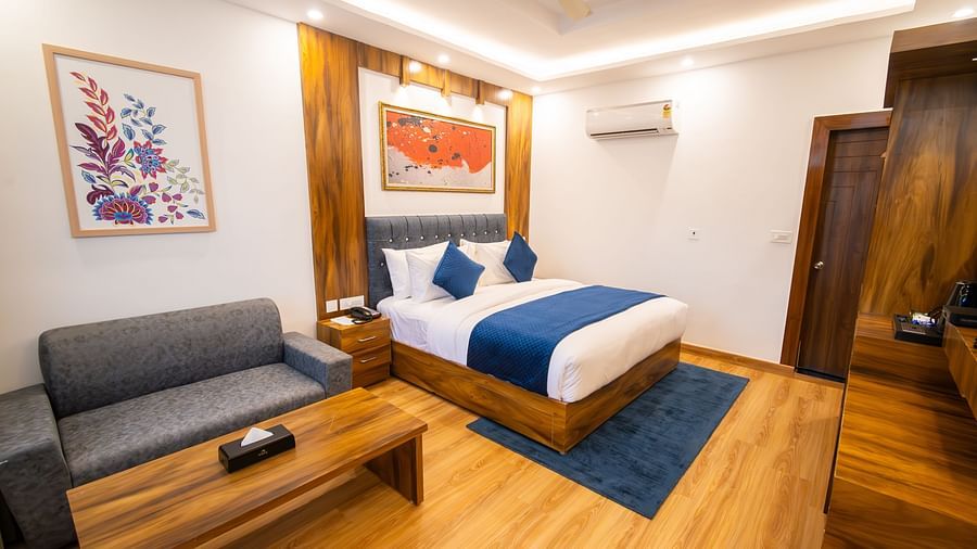 Shot of a air-conditioned room in the hotel featuring a king size bed, wooden furnishing, couch, wall paintings, and a table  | The Tattva Devprayag